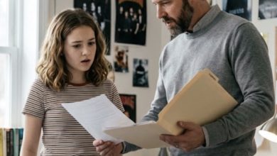 Photo of Create a highly realistic cinematic vertical 9:16 photograph inside a bright, modern American teenage bedroom.  A 13-year-old girl is standing beside her bed while talking seriously with her father, a well-dressed man in his early 40s. The father is holding a beige manila folder and several papers, showing one of the documents to his daughter while explaining something important. The girl looks surprised and uncertain as she looks at the papers.  Under the bed, partially concealed by the bed frame and blankets, the girl’s mother is quietly observing the conversation. Only part of the mother’s surprised face and her hand holding a smartphone are visible beneath the bed. The phone screen is illuminated as she holds it carefully.  The father and daughter are focused entirely on their conversation and do not notice the mother beneath the bed.  Create a strong sense of mystery and family drama without showing violence, physical confrontation, or threatening behavior.  Natural afternoon sunlight through the window, realistic teenage bedroom decorations, authentic American home, expressive faces, realistic skin texture, everyday clothing, cinematic photography, shallow depth of field, subtle dramatic atmosphere, photorealistic, candid documentary-style moment, one single continuous scene, no split screen, no collage, no text, no captions, vertical 9:16.